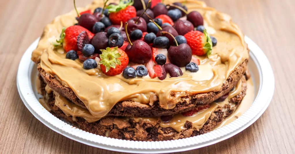 Delicious layered chocolate cake with fresh berries and peanut butter cream on a plate.