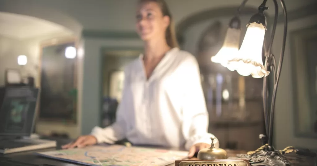 A concierge stands at a hotel reception desk under ambient lighting, ready to assist guests.