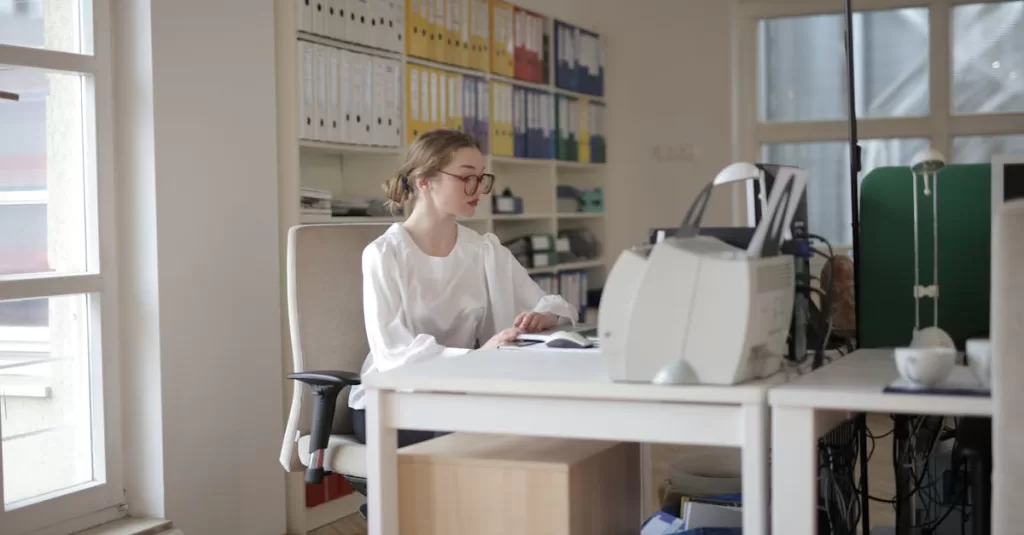 Focused woman working in a modern office filled with files and equipment.