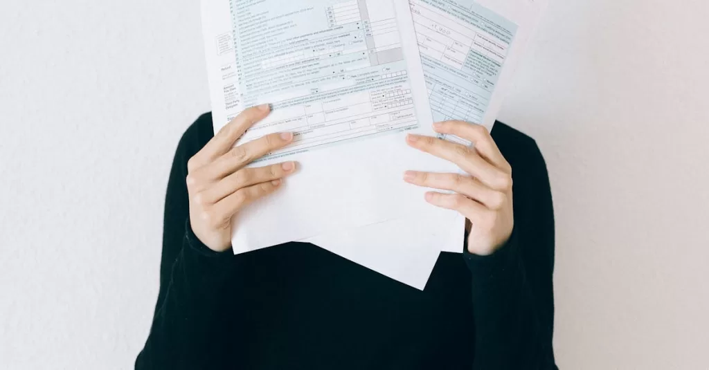 A woman concealing her face with tax forms, illustrating financial stress and paperwork burden.