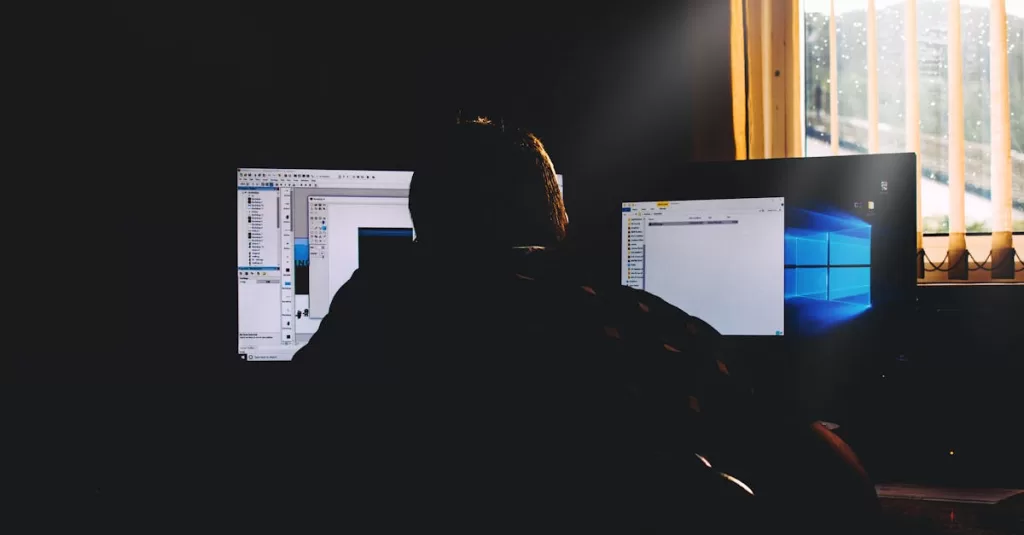 Silhouette of a person working on computers in a dimly lit office environment.