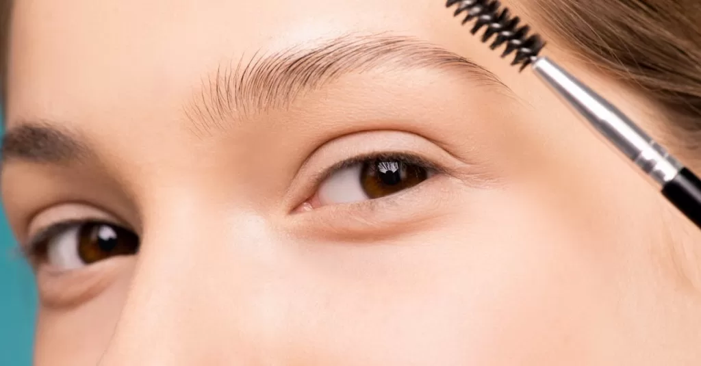 Close-up of a woman applying makeup with an eyebrow brush, highlighting natural beauty.