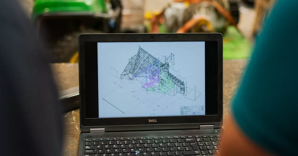 Two engineers reviewing architectural plans on a laptop in a busy workshop.