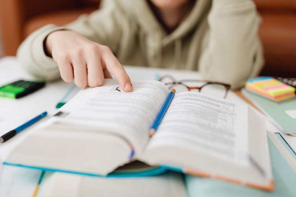 Focused student pointing at text in an open book, studying for exams indoors.